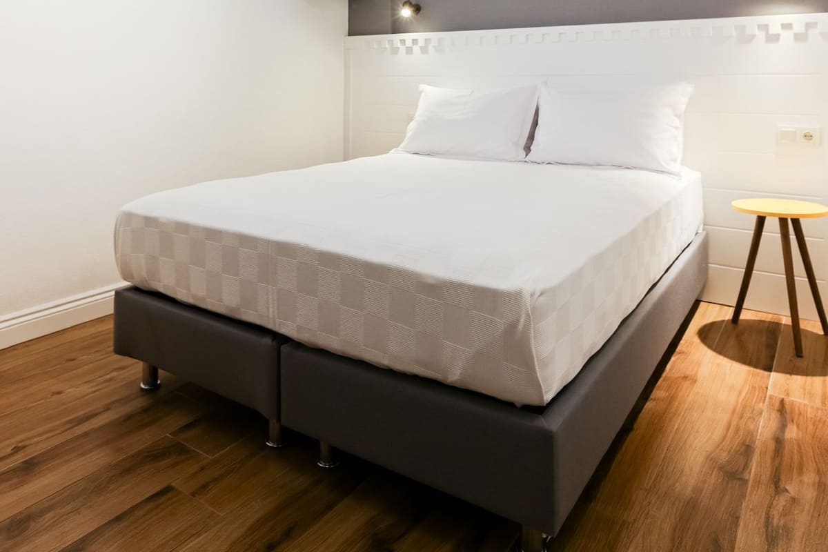 A modern bedroom with a bed, wooden flooring, a headboard, and a small table with a lamp.