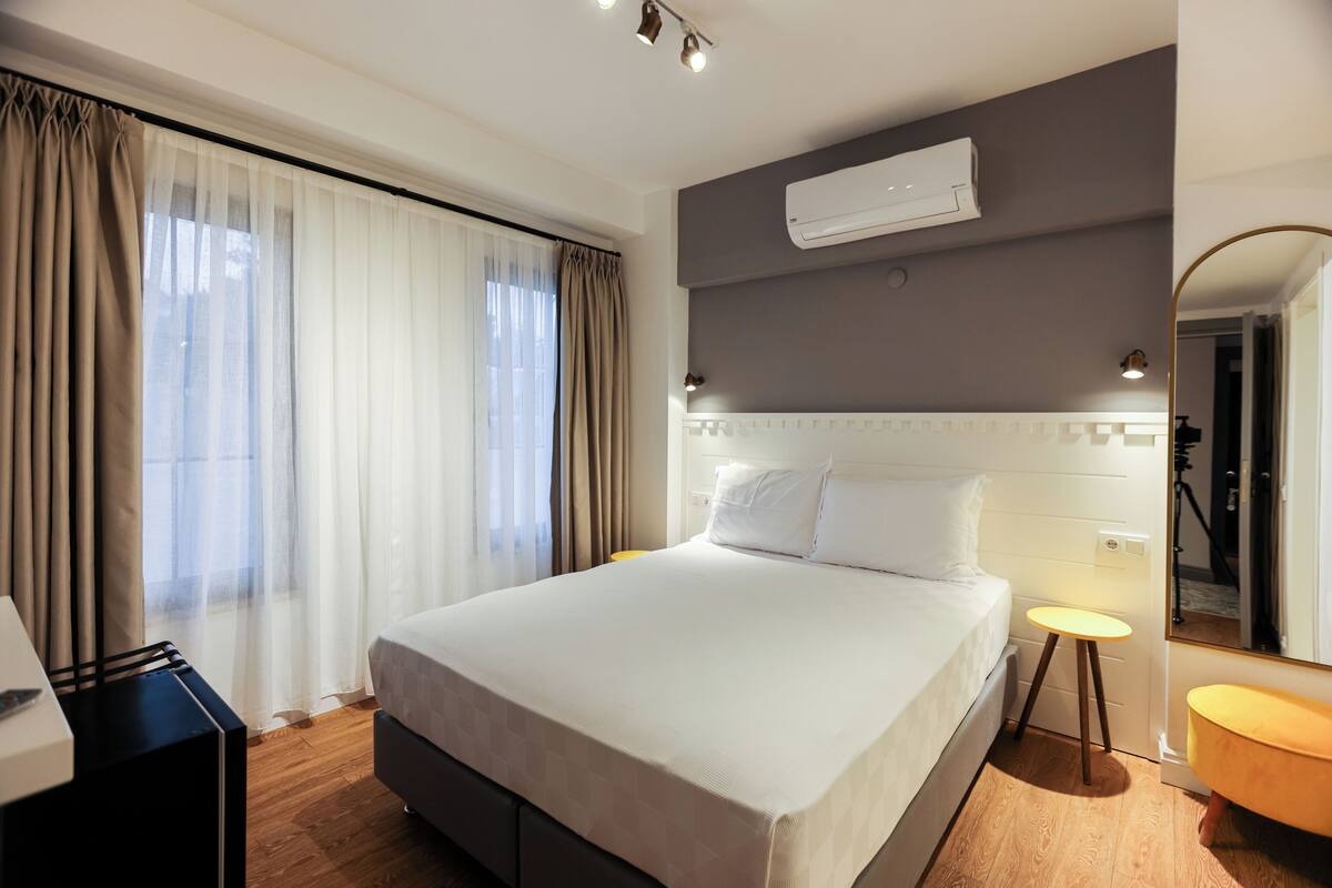 A hotel room with a large bed, a bedside table, a mirror, and an air conditioning unit.