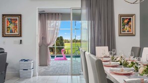 A dining area with a table set for four, a pink flamingo float in the background, and a view of a green landscape through a glass door.