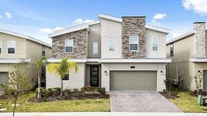 A modern two-story residential building with a garage, a small front yard with palm trees, and a clear sky.