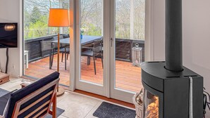 Una habitación con chimenea, televisor, zona de comedor con mesa y sillas, y vista a una terraza exterior a través de un ventanal.