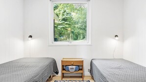 Una habitación pequeña con dos camas, una ventana que ofrece vistas a zonas verdes, una mesita de noche con lámpara y un enchufe.