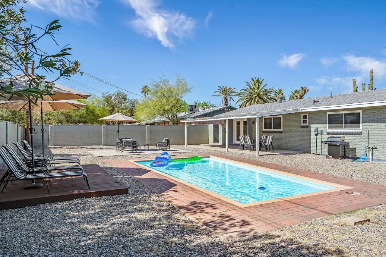 A backyard with a swimming pool, lounge chairs, and a barbecue area.