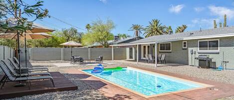 A backyard with a swimming pool, lounge chairs, and a barbecue area.