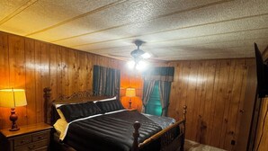 Ein Schlafzimmer mit Holzboden, einem Bett mit Kopfteil, zwei Nachttischen mit Lampen und einem Deckenventilator.
