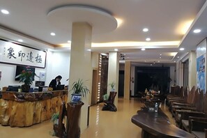 Un vestíbulo de hotel con mostrador de recepción, sillas y mesas de madera.