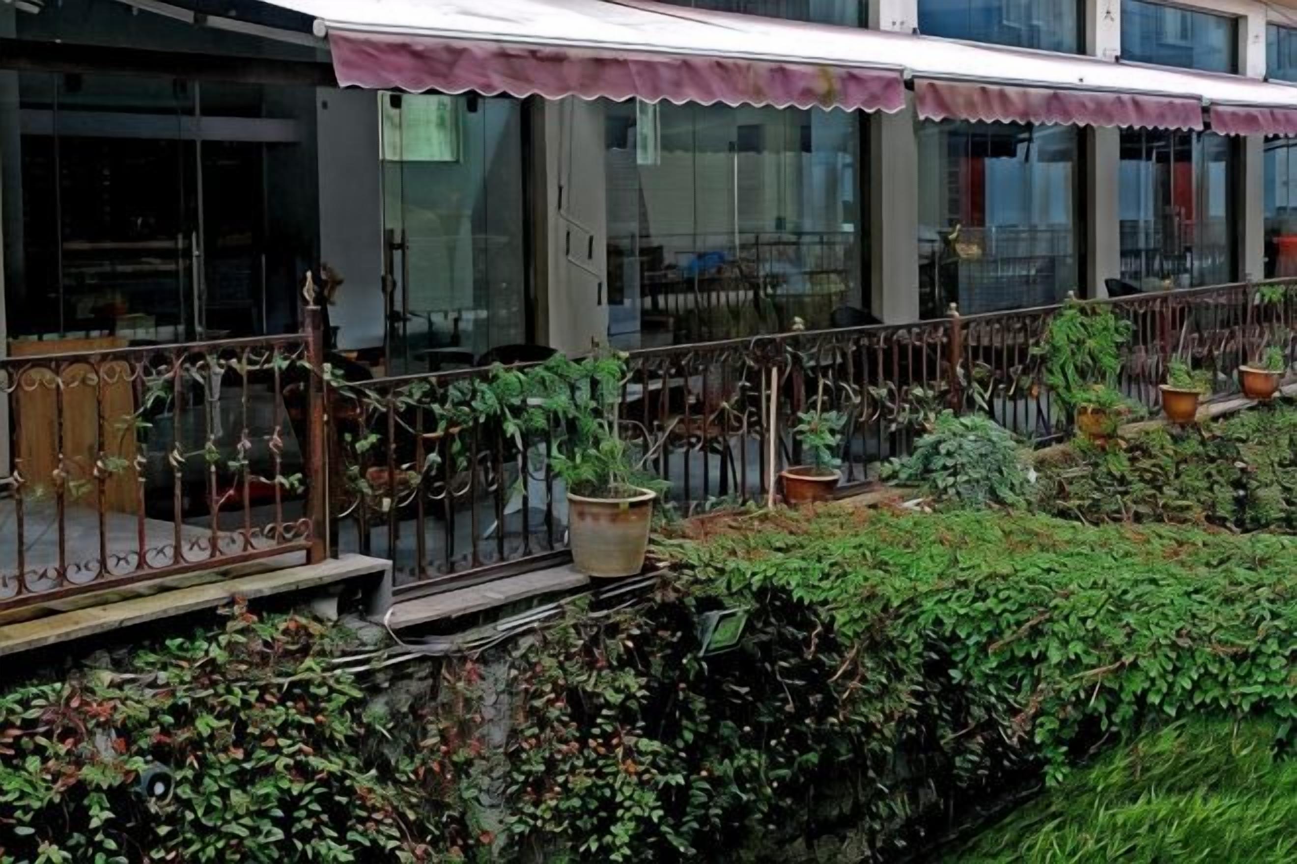 Un edificio con un espacio exterior techado, plantas en macetas y una barandilla de metal.
