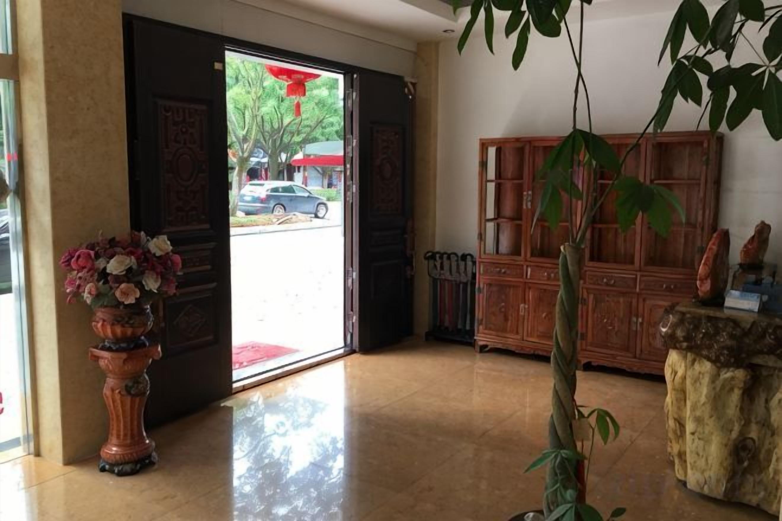 A hotel lobby with a wooden cabinet, a potted plant, and a large vase of flowers.