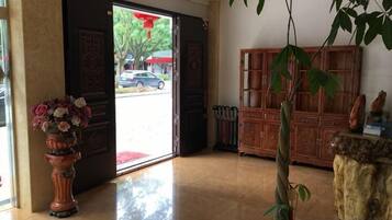 A hotel lobby with a wooden cabinet, a potted plant, and a large vase of flowers.