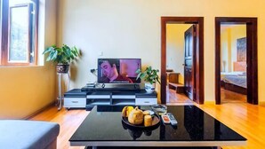 A living room with a TV, a coffee table with snacks, a sofa, and a potted plant.