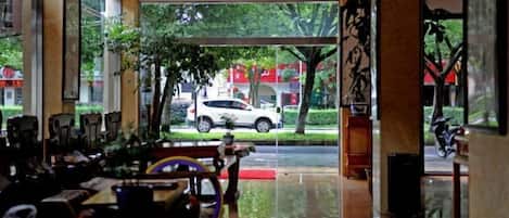 A hotel lobby with a view of a street, a reception desk, and a seating area.