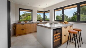 Een moderne keuken met houten kastjes, een centraal eiland en grote ramen met uitzicht op groen.