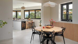 Een moderne keuken met een centraal eiland, grote ramen en een eethoek met een ronde tafel en stoelen.