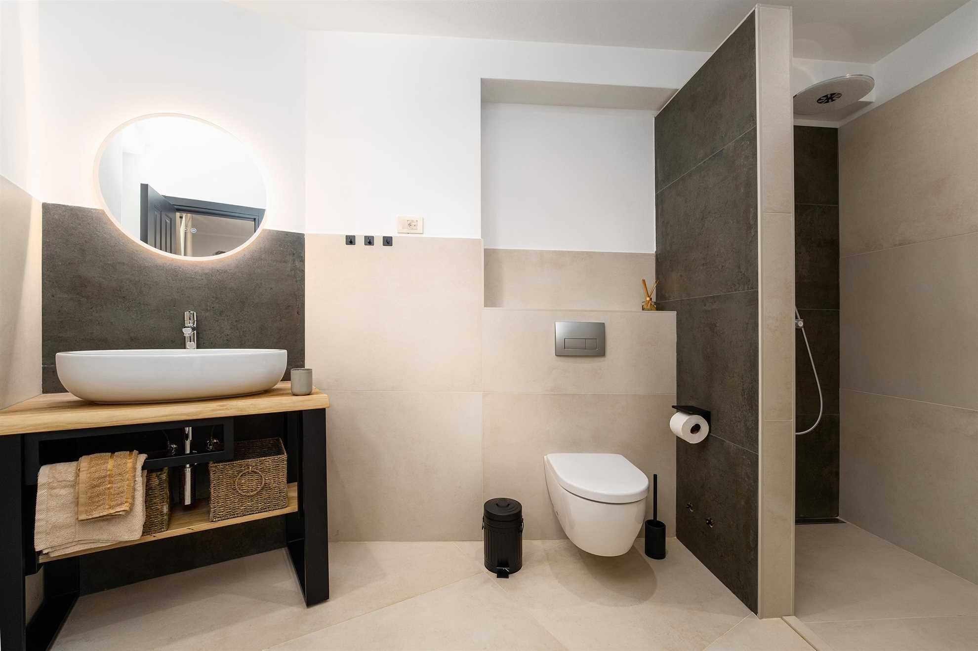 A modern bathroom with a round mirror, a sink, a toilet, and a shower area.