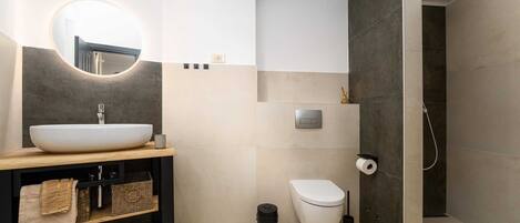 A modern bathroom with a round mirror, a sink, a toilet, and a shower area.