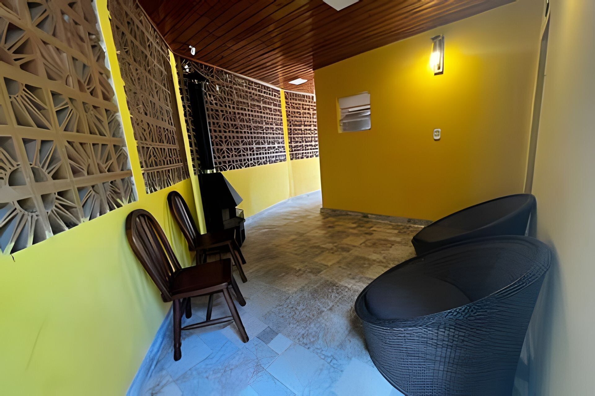A room with yellow walls, a wooden ceiling, and a tiled floor. There are two chairs and a sofa.