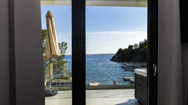Un balcón con vista al mar, un jacuzzi y una sombrilla.