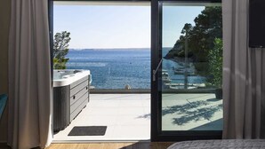 Una habitación con puerta de vidrio corredera que da a un balcón con vistas al mar y una bañera de hidromasaje.