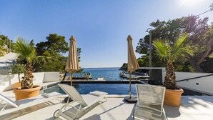 Zona de piscina en la azotea con sillones de descanso y sombrillas, con vistas a un puerto deportivo y al mar.