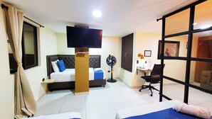 Una habitación de hotel con cama, escritorio, silla, televisor y ventilador.