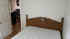 Un dormitorio con cabecera de madera, colcha blanca acolchada y una puerta que da a otra habitación.