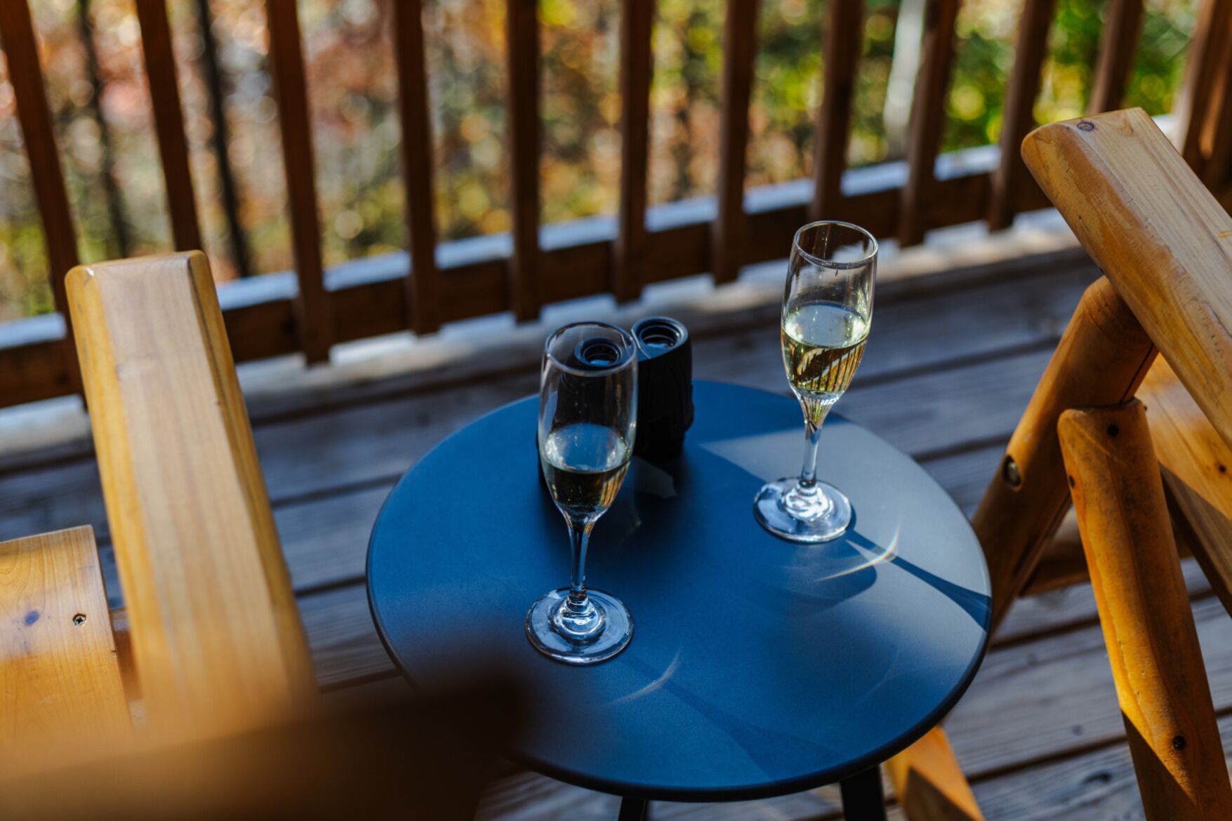 A wooden deck with a small round table, two glasses of white wine, and a bottle of water.