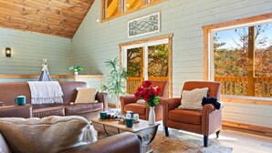 Un salon chaleureux avec un plafond en bois, une grande fenêtre donnant sur les arbres et une cheminée.