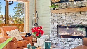 Un espace extérieur accueillant, doté d’une cheminée en pierre, d’une terrasse en bois et offrant une vue sur les arbres.