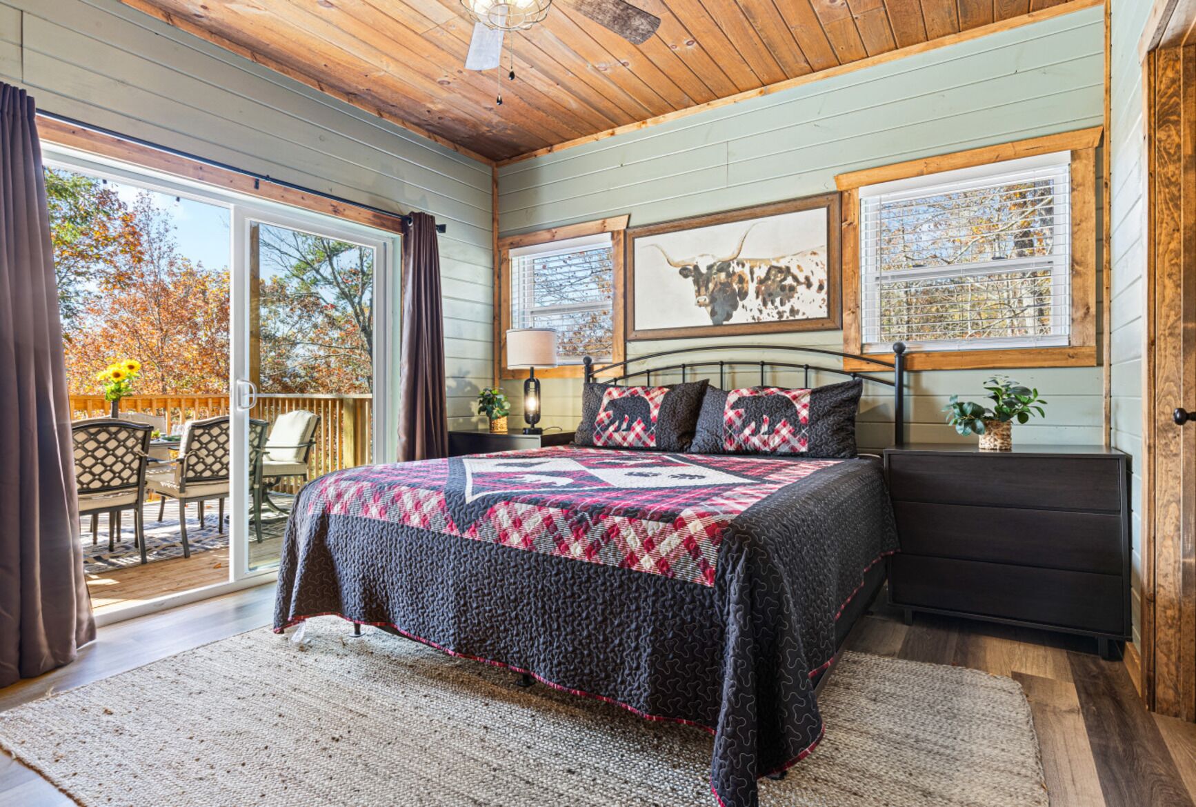 Un dormitorio con cama, mesita de noche, lámpara y ventana que muestra una vaca.