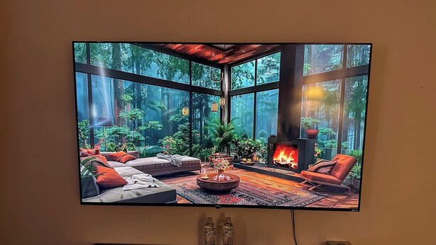 A flat-screen TV displaying a forest scene with a fireplace, sofas, and a coffee table. - Cherry's Villa 14 (Grants Pass)