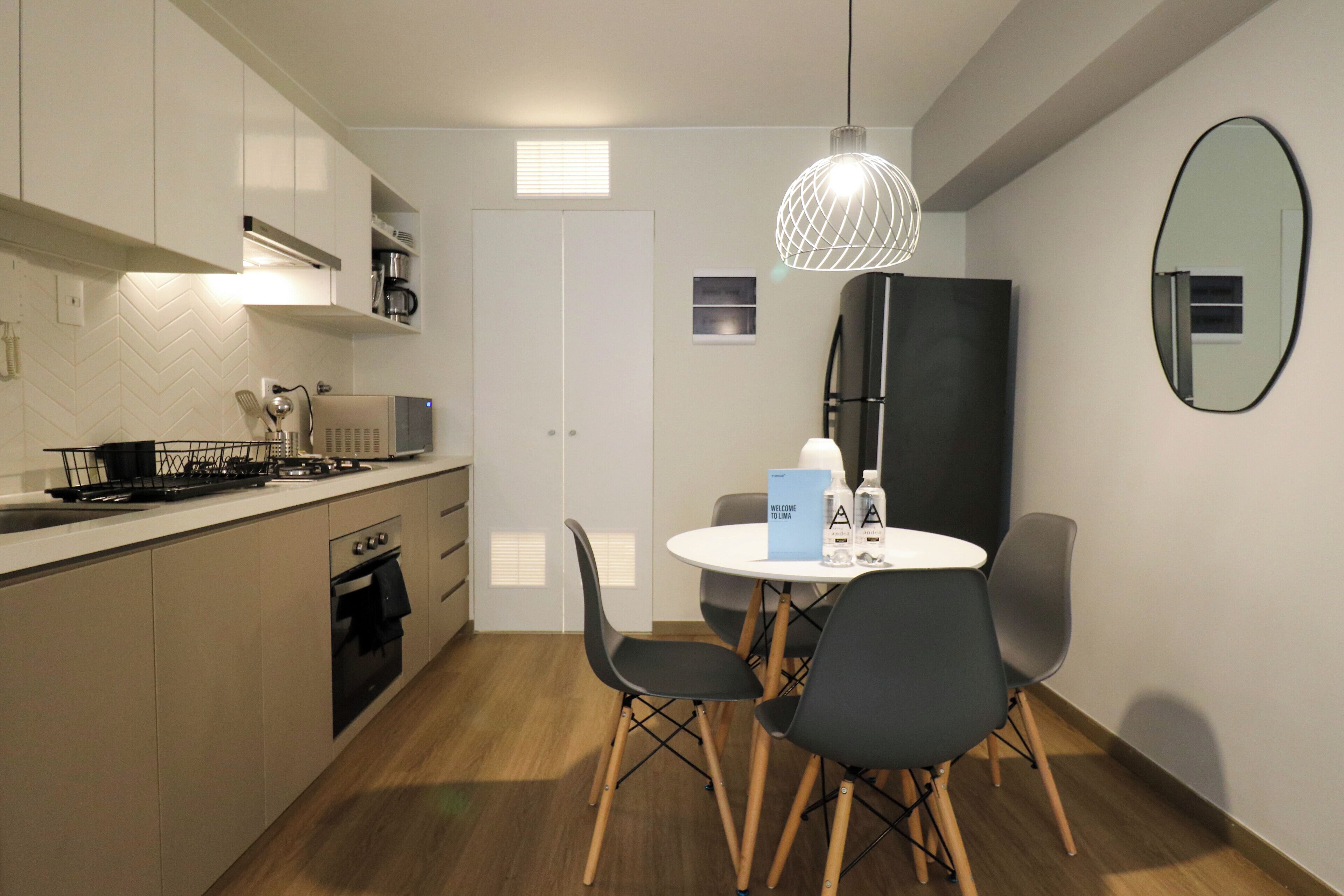 A modern kitchen with a dining area, including a round table with chairs, a black refrigerator, and a hanging light fixture.