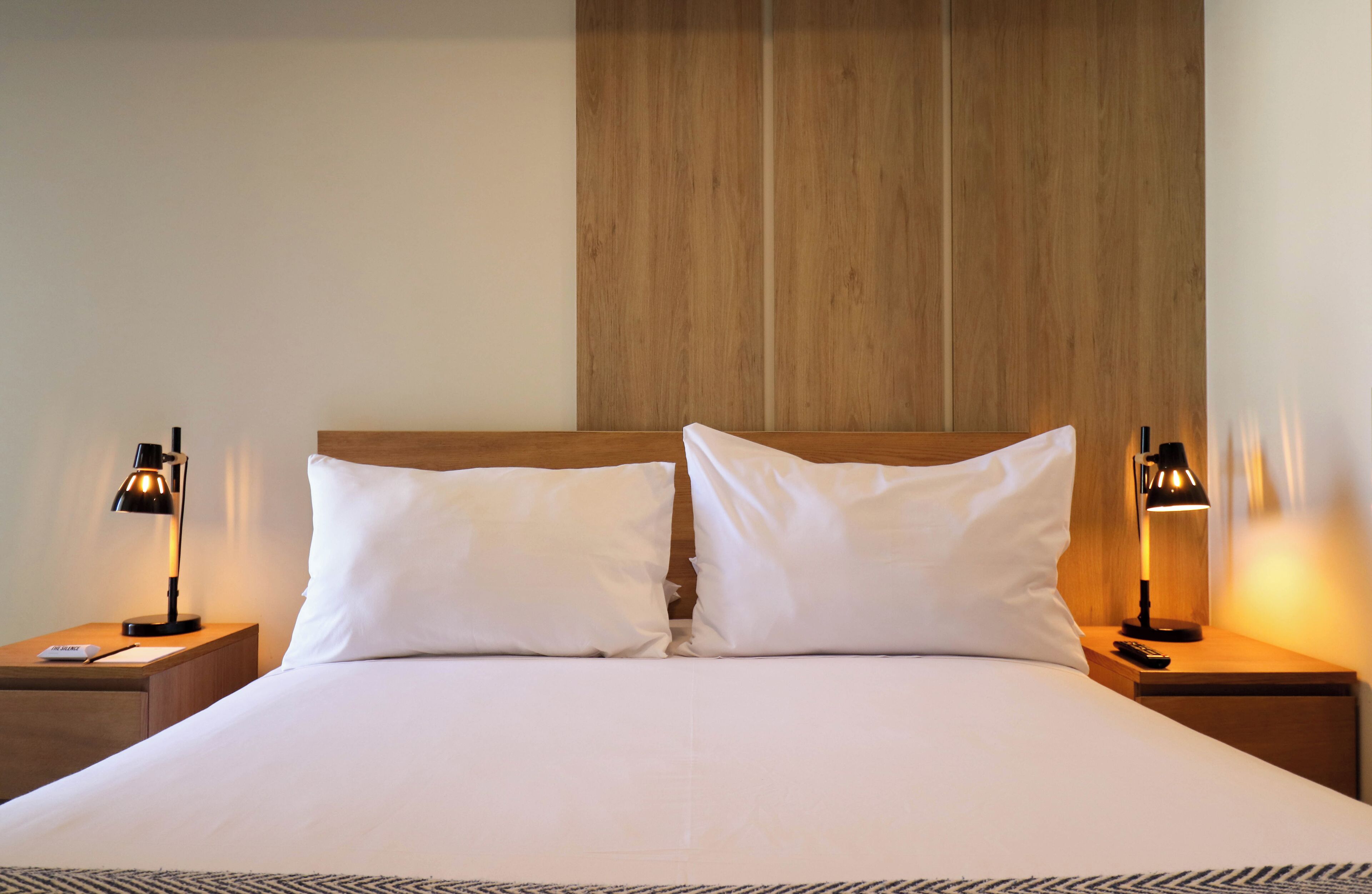 A neatly made bed with white linens and two bedside lamps on wooden nightstands.