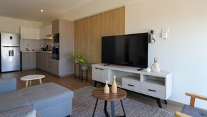 A modern living room with a grey sofa, a coffee table, a TV on a stand, and a kitchen in the background. - La Mar Miraflores by Wynwood House (Lima)