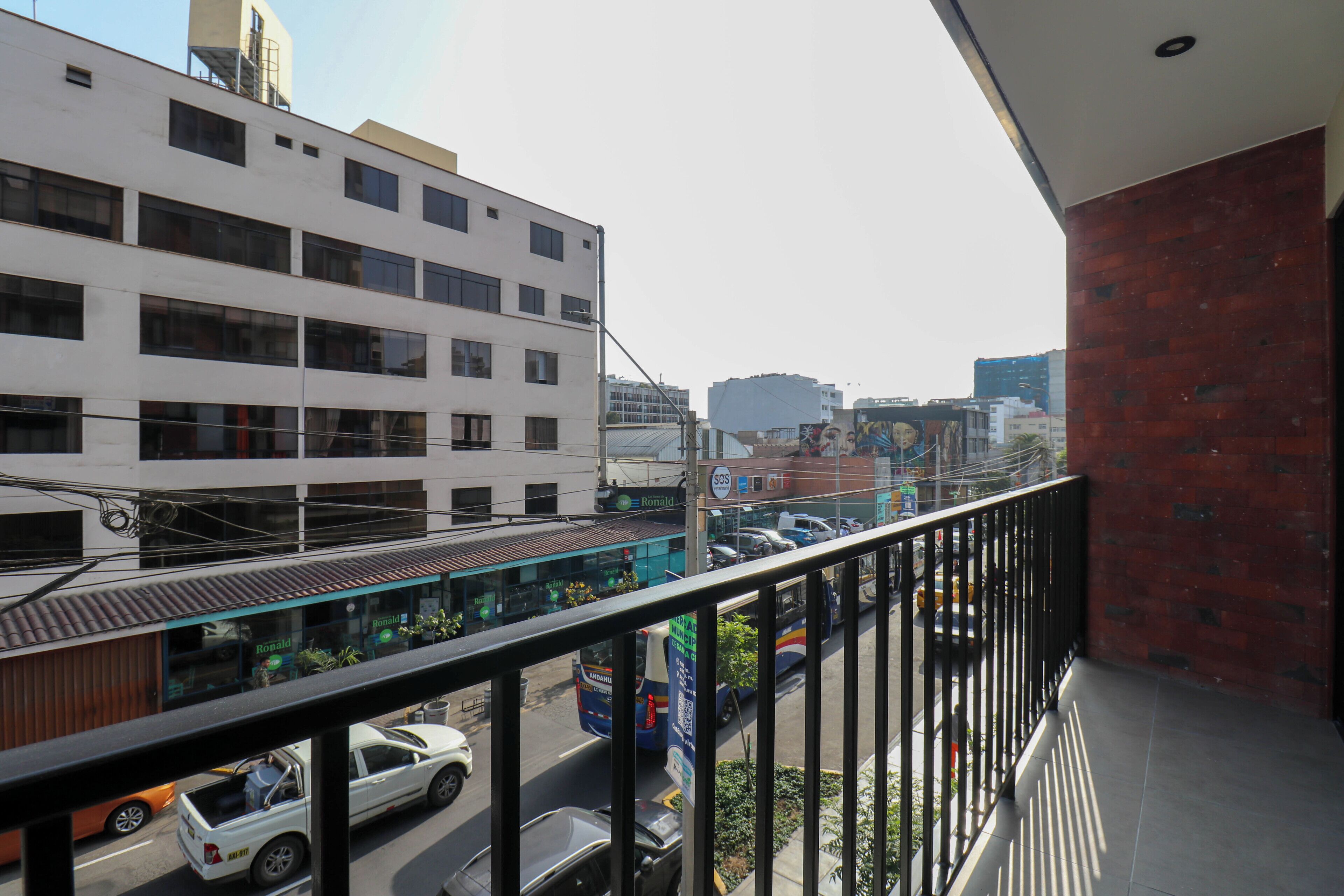 A balcony with a view of a busy street, a building with multiple windows, and a clear sky.