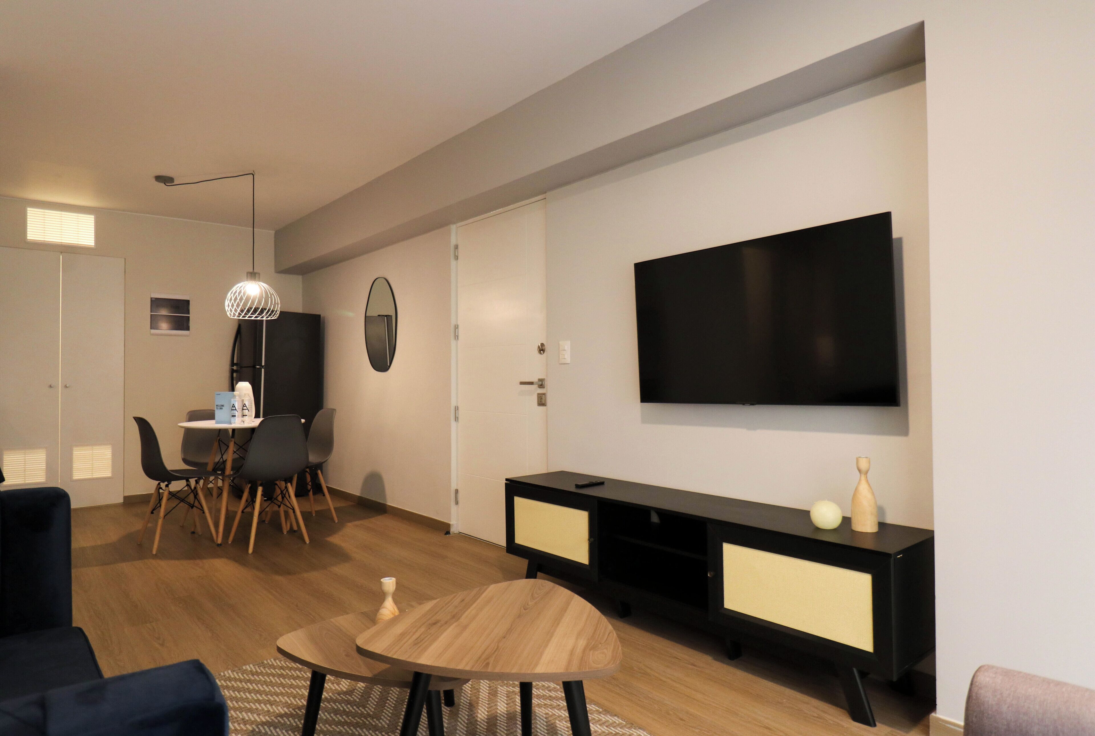 Un salon moderne doté d’un téléviseur à écran plat, d’un coin repas avec une table et des chaises, et d’un meuble de rangement noir pour les appareils multimédias.