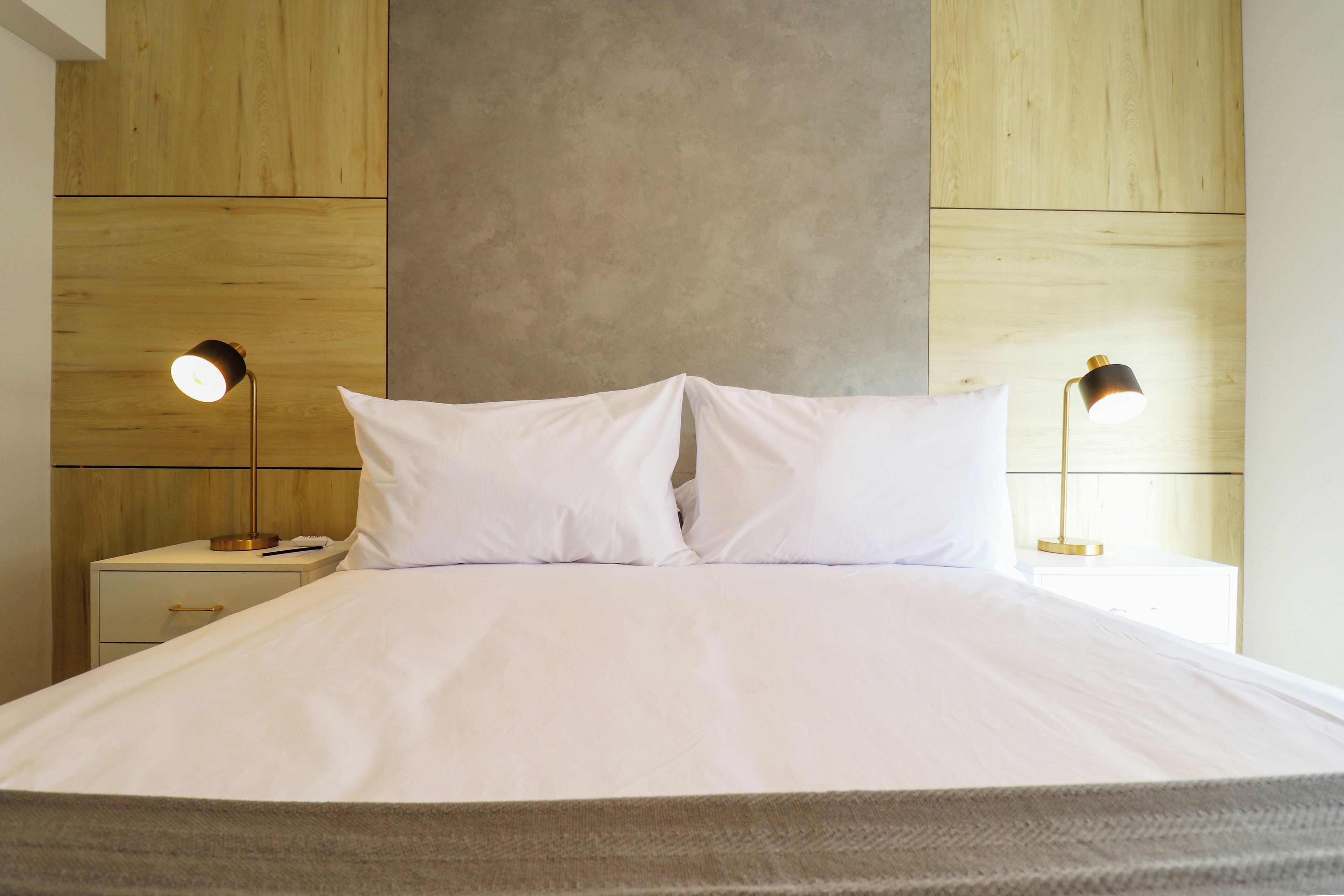 Una cama bien hecha con sábanas blancas, dos lámparas de noche y un cabecero de madera.