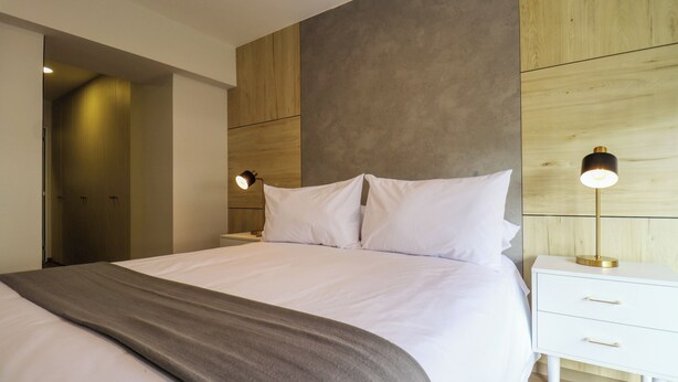 A modern bedroom with a large bed, a bedside table with a lamp, and a wooden accent wall. - La Mar Miraflores by Wynwood House (Lima)