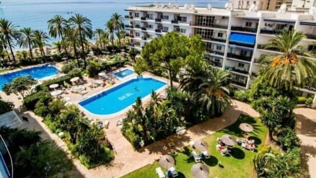 Un hotel con piscina, palmeras y vistas al mar.