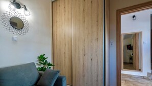 Een kamer met een houten garderobe, een blauwe bank, een kamerplant en een spiegel aan de muur.