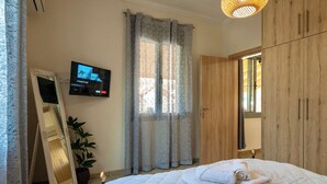 Een slaapkamer met een bed, een aan de muur bevestigde televisie, een garderobe en een spiegel.