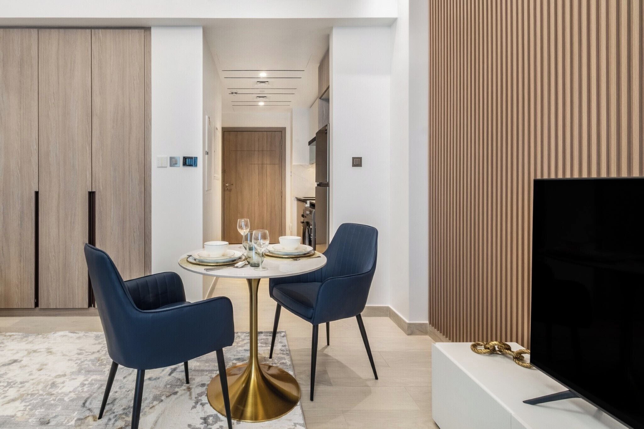 A modern dining area with a round table, two blue chairs, and a gold base.