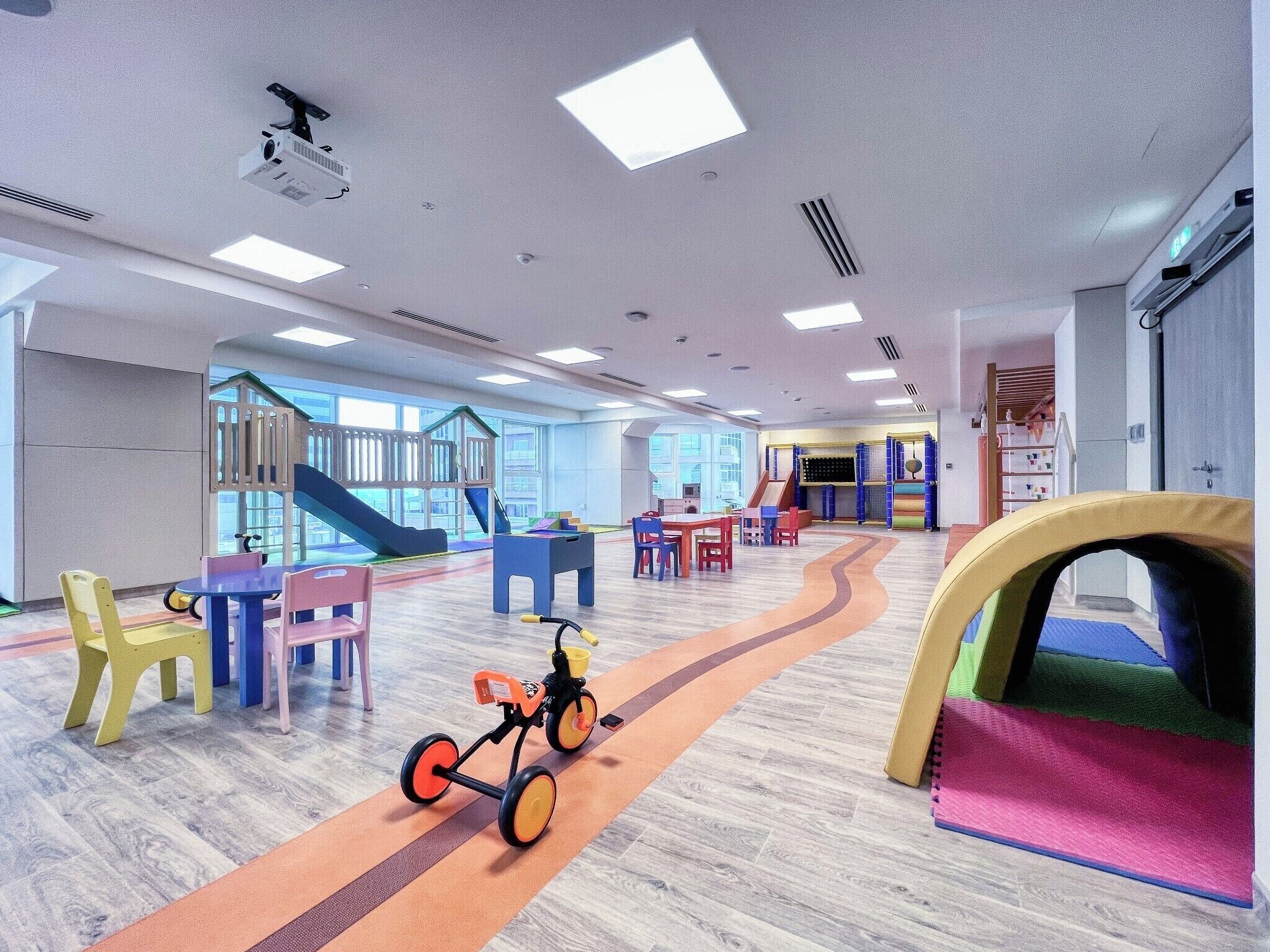 A spacious indoor play area with a slide, play structures, and a tricycle path.
