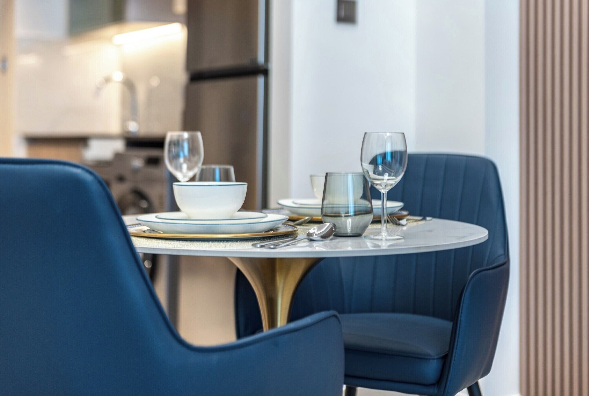 A dining area with a round table set for two, featuring blue upholstered chairs and a white tablecloth.