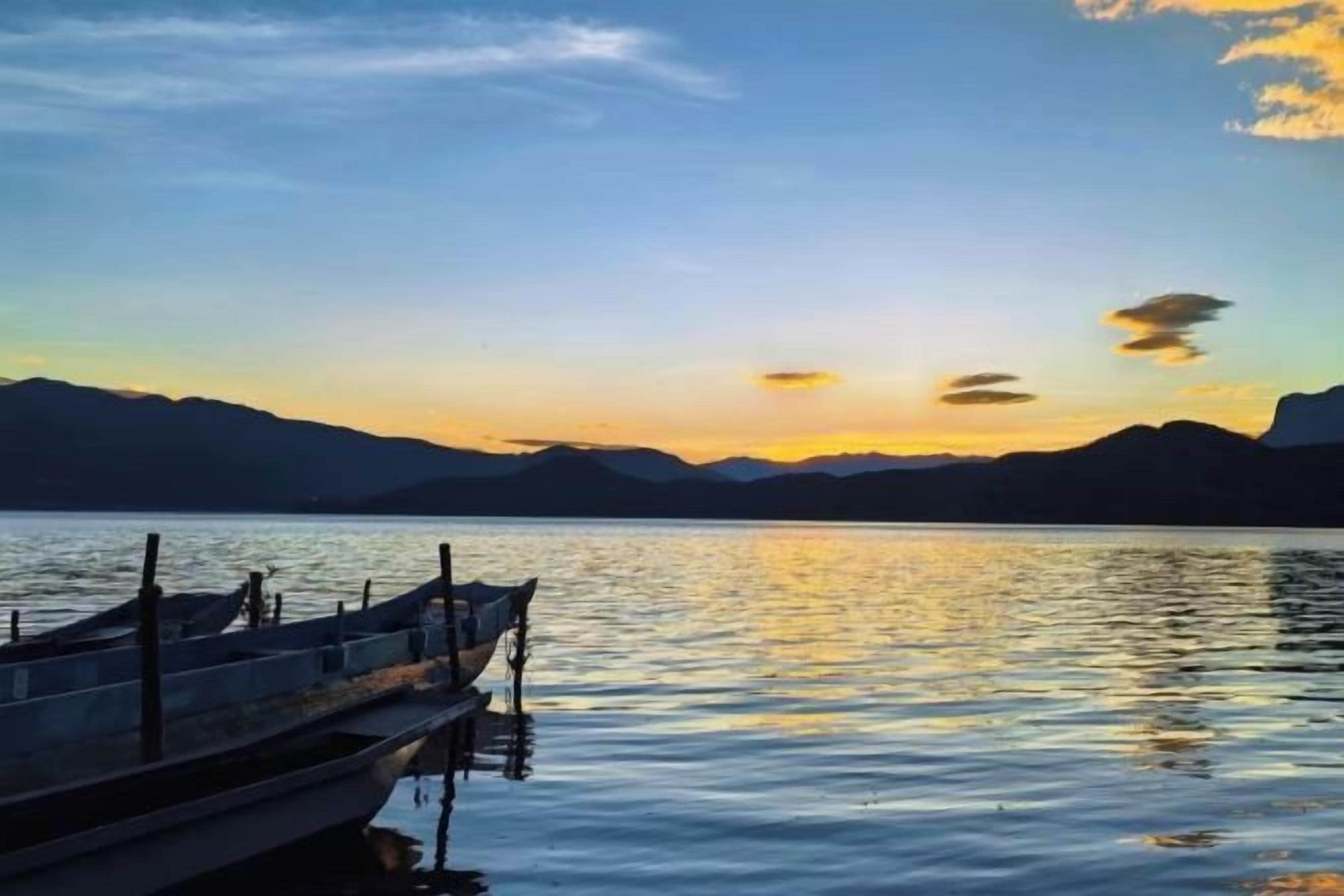 A calm lake at sunset with a boat docked on the left.