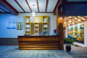 A reception desk with a wooden counter, a potted plant, and a painting on the wall. - Lugu Manor Hotel (Ninglang)