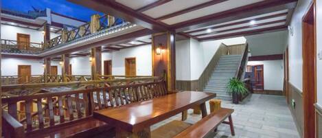 A spacious hall with a long wooden table and benches, a staircase, and a balcony.