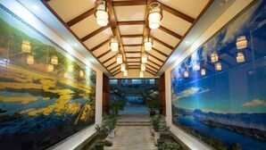 A corridor with a high ceiling, wooden beams, and a mural on the walls depicting a landscape. - Lugu Manor Hotel (Ninglang)