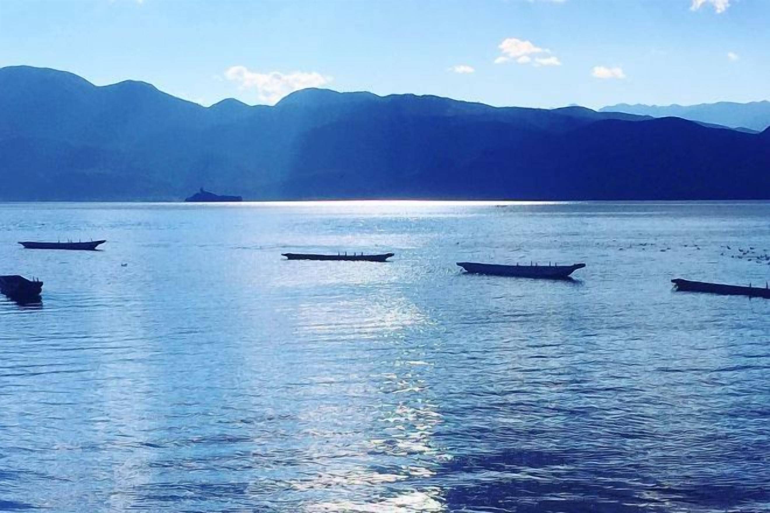 A calm body of water with several boats and distant mountains.