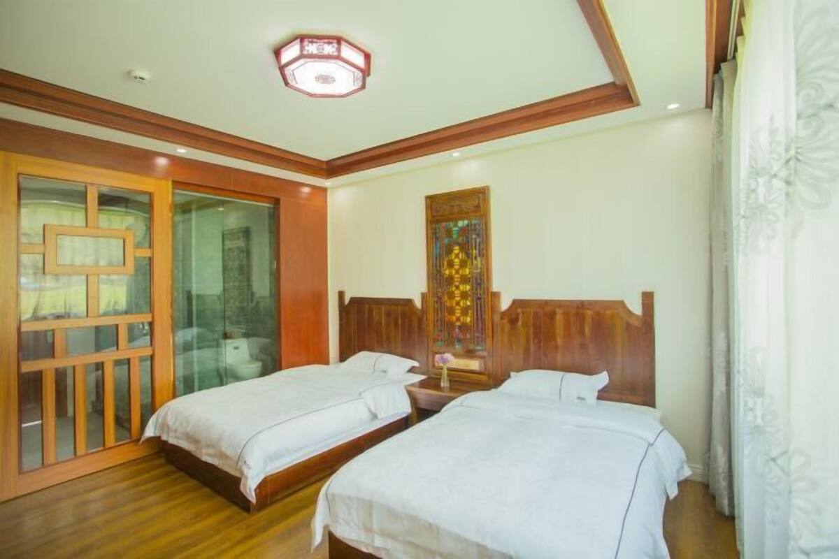 A hotel room with two single beds, a wooden headboard, a glass door, and a decorative wall piece.