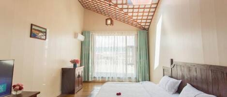 Habitación de hotel con techo de madera, cama con ropa blanca, televisor sobre un mueble de madera y ventana con cortinas.